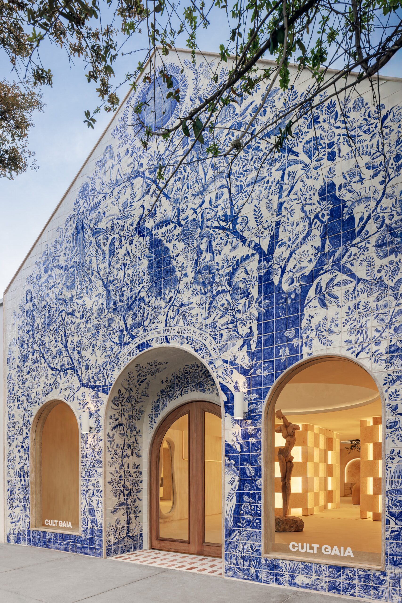 the facade of a fashion boutique completely covered in hand-painted blue tile featuring an elaborate tree of life motif with flowers and birds