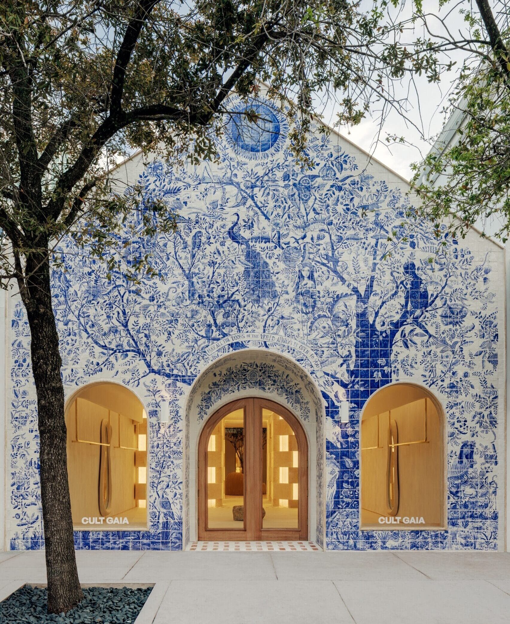 the facade of a fashion boutique completely covered in hand-painted blue tile featuring an elaborate tree of life motif with flowers and birds