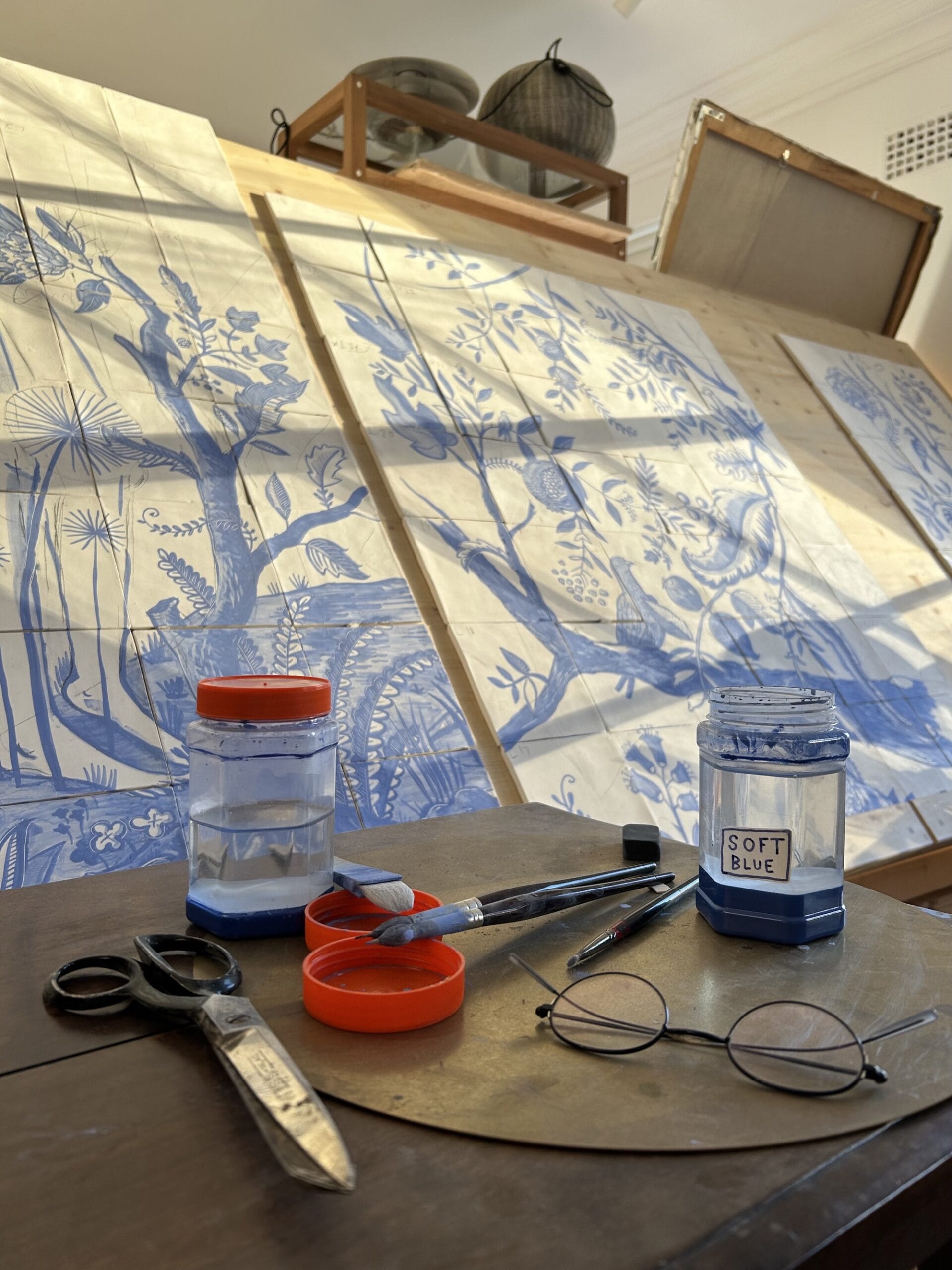 sections of ceramic tile painted with blue glaze, propped up on a surface with art materials in the foreground