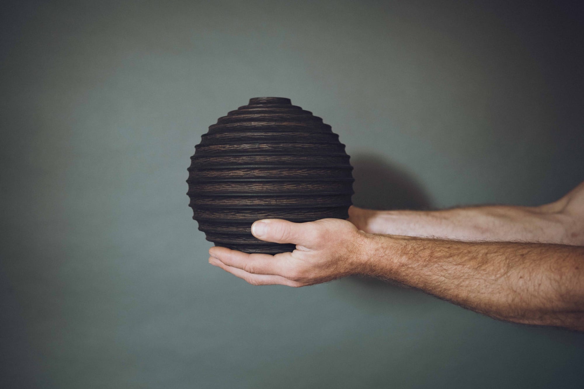 a handmade wooden vessel held in front of a gray background in someone's hands