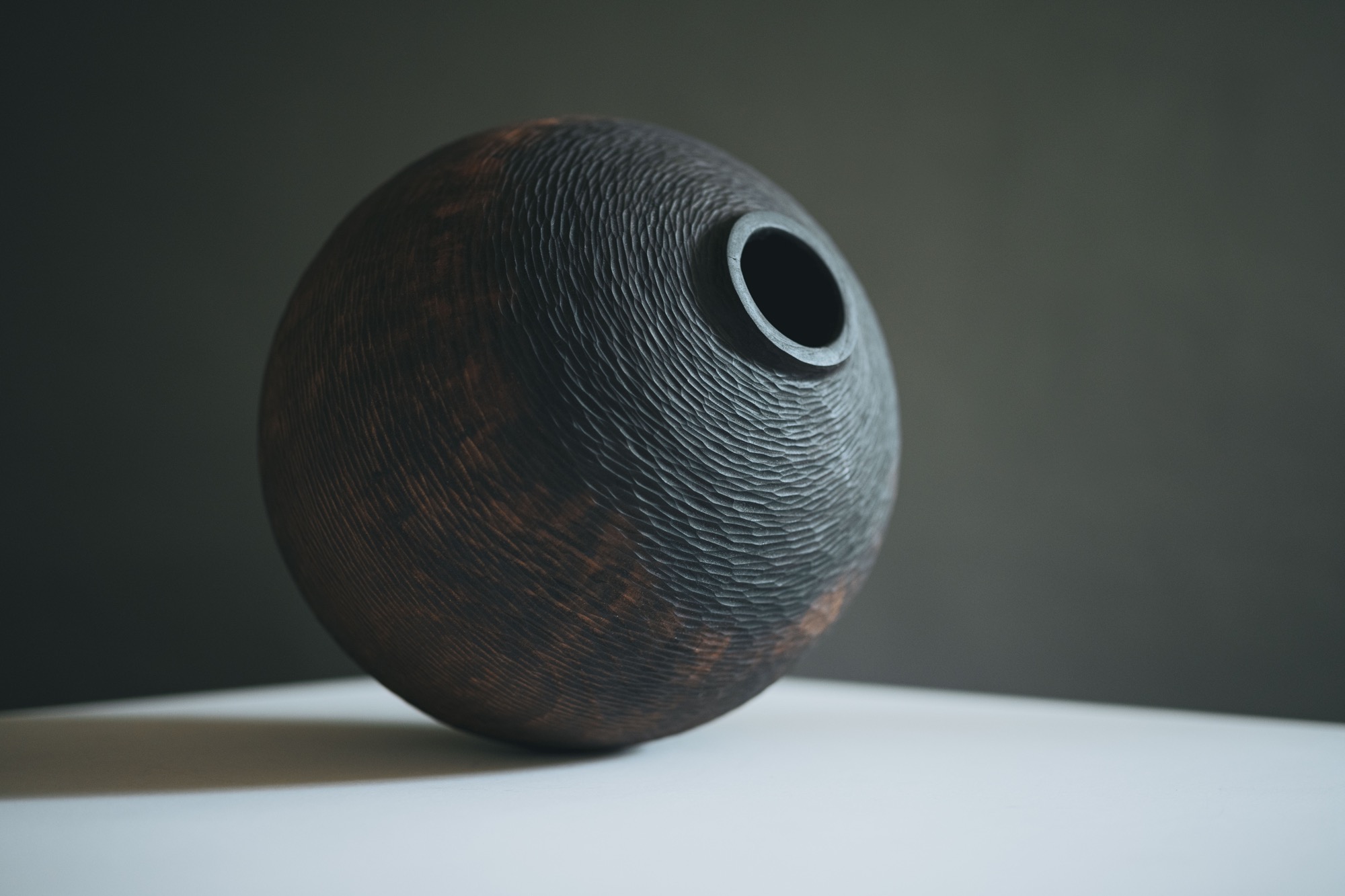 a handmade wooden vessel with a scored surface, illuminated against a dark background