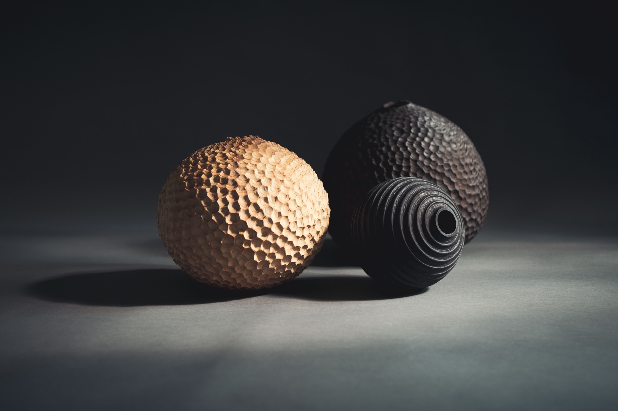 a collection of three handmade wooden vessels with faceted surfaces, illuminated against a dark background