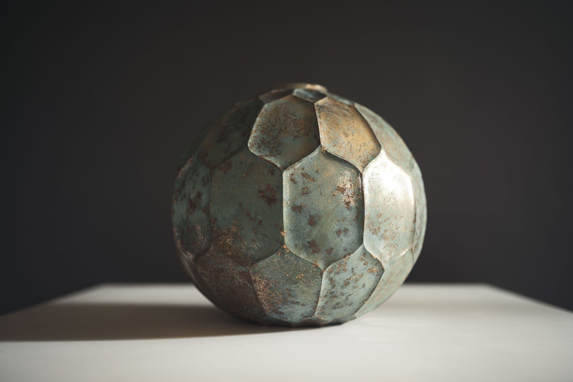 a bronze vessel with a faceted surface, illuminated against a dark background