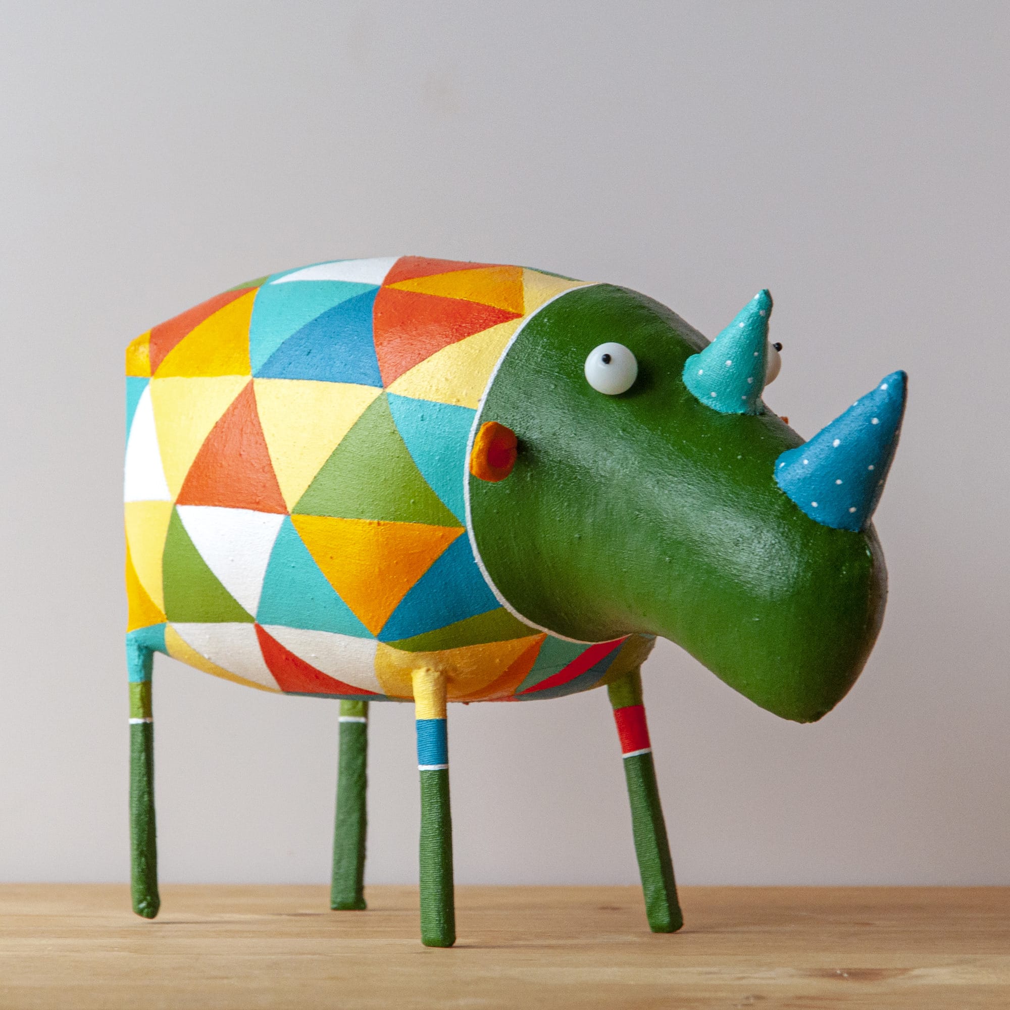 a wide-eyed green rhinoceros with blue polka-dot horns wears a colorful geometric sweater.