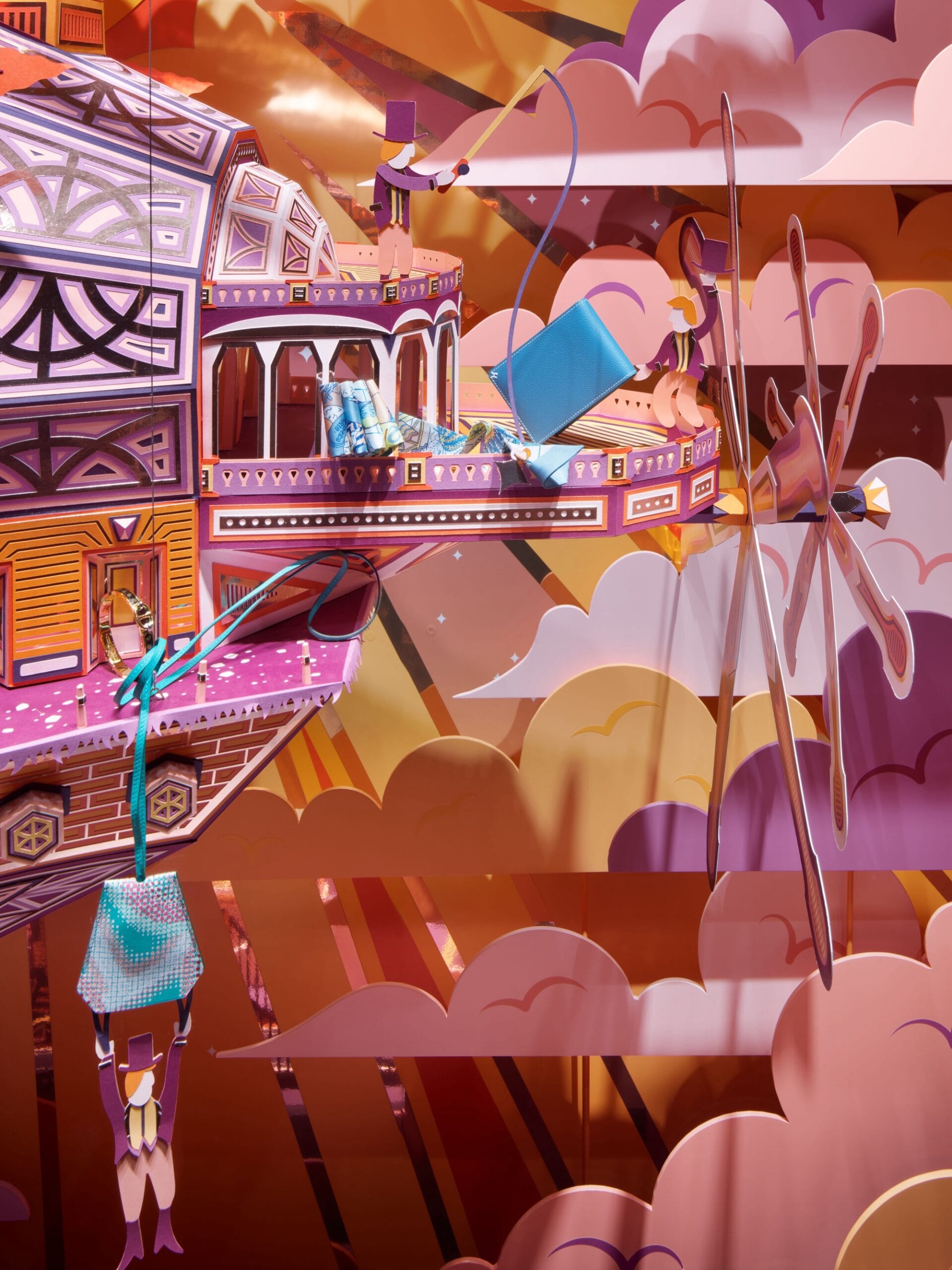 a detail image of a man in a top hat hanging from a luxury hermes tag that's fastened to a large paper ship that appears to fly among pink, purple, and orange clouds