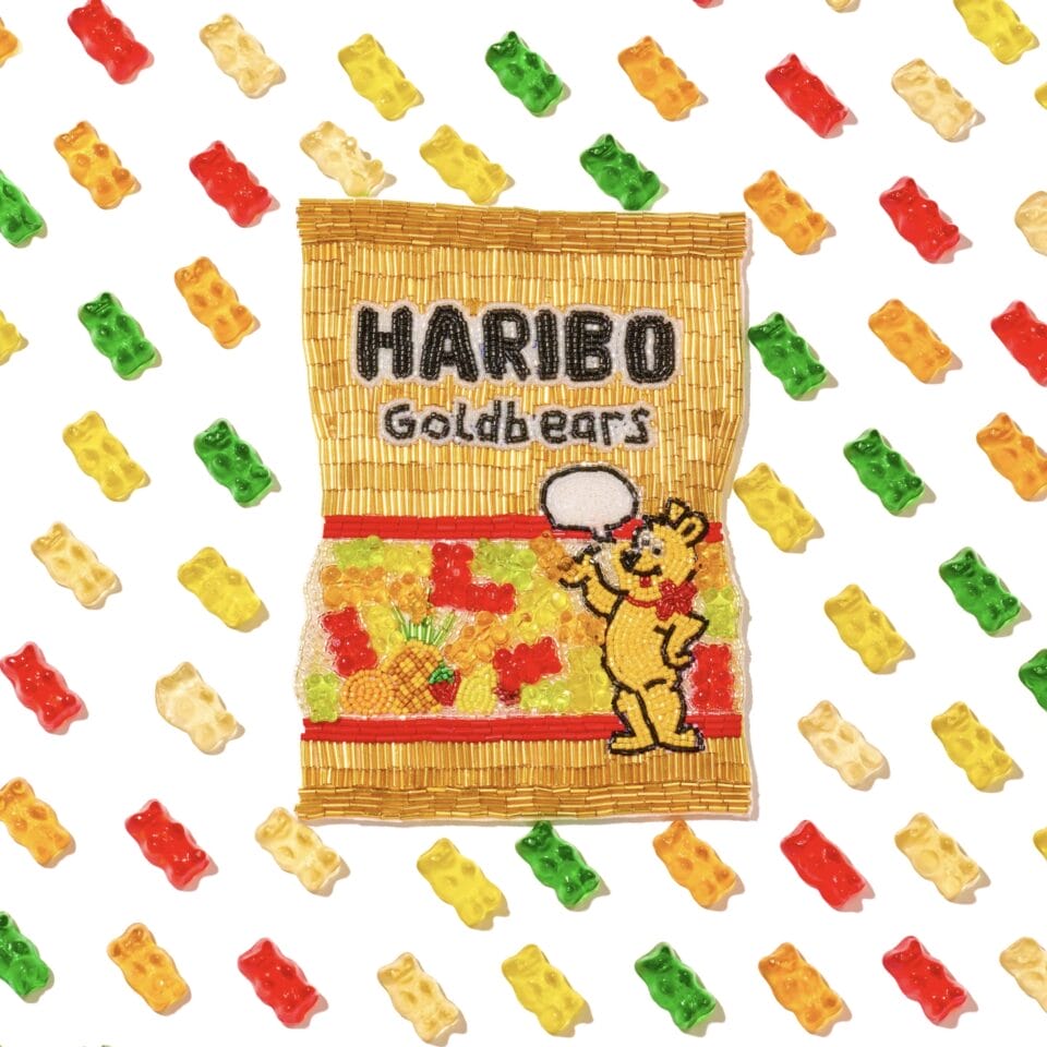 a beaded depiction of a bag of Haribo gummy bears. A pattern of diagonal gummy bears appears in the background.