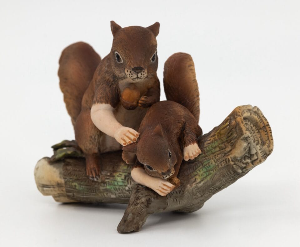 a reimagined secondhand ceramic kitsch piece of two squirrels on a log with both animals given human arms